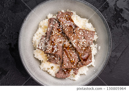 Yakiniku, wagyu marbled beef cuts and rice in a bowl. A culinary journey that captures the essence of Japanese grilling traditions. black background. top view Yakiniku, wagyu marbled beef cuts and rice in a bowl. A culinary journey that captures the essence of Japanese grilling traditions. black background. top view 130805964
