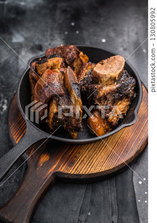 Tender beef short ribs in a pan, seasoned with herbs and spices. Perfect for culinary blogs or restaurant menus that focus on hearty, flavorful meat dishes. black background. top view Tender beef short ribs in a pan, seasoned with herbs and spices. Perfect for culinary blogs or restaurant menus that focus on hearty, flavorful meat dishes. black background. top view 130805992