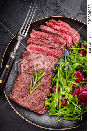 Grilled and sliced Flank beef steak on plate with salad. black background. top view 130806056