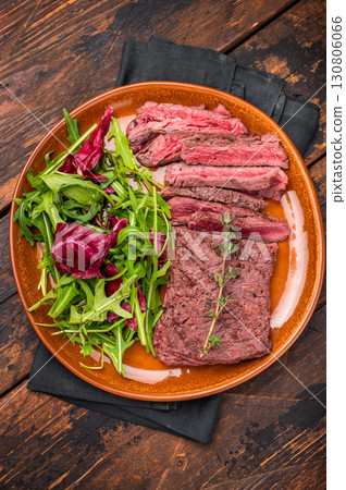 Grilled Skirt machete beef steak, roasted sliced meat on plate with salad. wooden background. top view Grilled Skirt machete beef steak, roasted sliced meat on plate with salad. wooden background. top view 130806066
