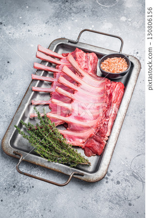 Raw mutton meat for chops steaks, uncooked rack of lamb on steel tray with herbs. grey background. top view Raw mutton meat for chops steaks, uncooked rack of lamb on steel tray with herbs. grey background. top view 130806156