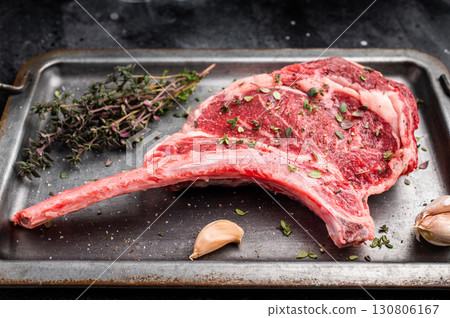 Ready for cooking Tomahawk beef steak with seasonings, raw marbled rib eye with bone on steel tray. black background. top view Ready for cooking Tomahawk beef steak with seasonings, raw marbled rib eye with bone on steel tray. black background. top view 130806167