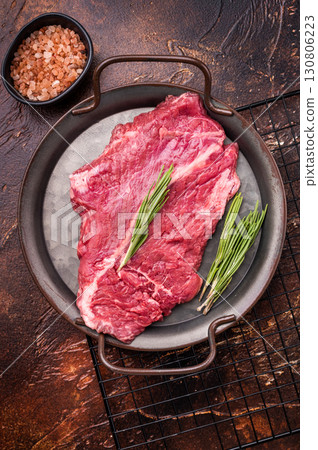 Raw hanger tender beef steak, skirt steak with rosemary on steel tray. brown background. top view Raw hanger tender beef steak, skirt steak with rosemary on steel tray. brown background. top view 130806223
