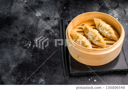 Steamed Japanese Gyoza Dumplings with pork meat and vegetables in bamboo steamer. black background. top view Steamed Japanese Gyoza Dumplings with pork meat and vegetables in bamboo steamer. black background. top view 130806540