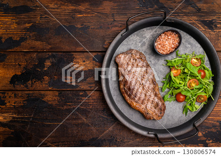 Grilled striploin steak, strip loin beef meat steak on a steel tray. wooden background. top view Grilled striploin steak, strip loin beef meat steak on a steel tray. wooden background. top view 130806574