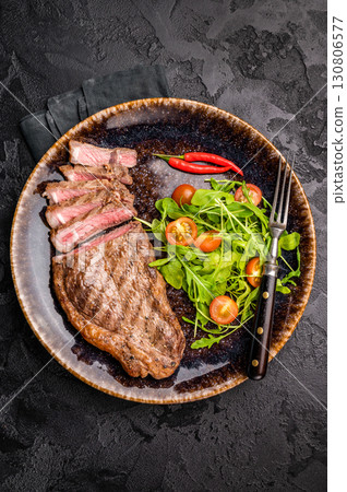 Grilled striploin steak, beef meat steak on a plate with salad. black background. top view Grilled striploin steak, beef meat steak on a plate with salad. black background. top view 130806577