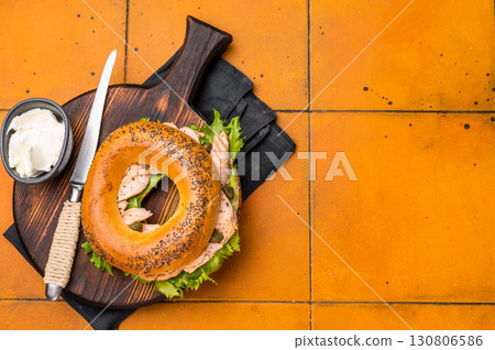 Breakfast Bagel with smoked salmon, lettuce and cream cheese on a wooden board. orange background. top view Breakfast Bagel with smoked salmon, lettuce and cream cheese on a wooden board. orange background. top view 130806586