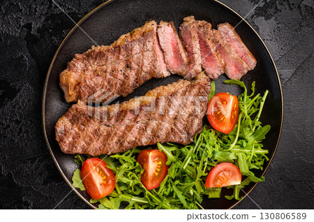 Grilled Steak from Black Angus beef meat on a plate with salad. black background. top view 130806589