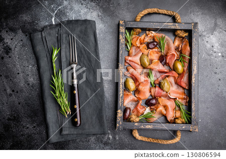 Prosciutto ham or Jamon Serrano with rosemary and olives in wooden tray. black background. top view 130806594