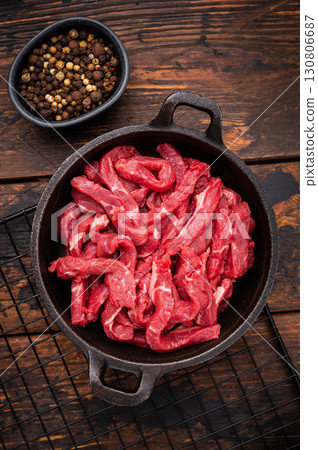 Raw beef meat sliced strips for beef stroganoff in a skillet. wooden background. top view Raw beef meat sliced strips for beef stroganoff in a skillet. wooden background. top view 130806687