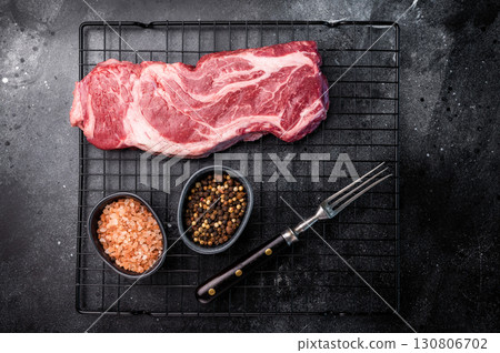 Ready for cooking Chuck eye roll steak, fresh raw beef meat on a rack. black background. top view 130806702