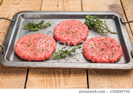 Raw hamburger minced meat patties for burgers with herbs on tray. wooden background. top view Raw hamburger minced meat patties for burgers with herbs on tray. wooden background. top view 130806740