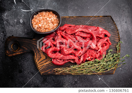 Uncooked Raw beef sliced meat, strips for cooking beef stroganoff on wooden board. black background. top view 130806761