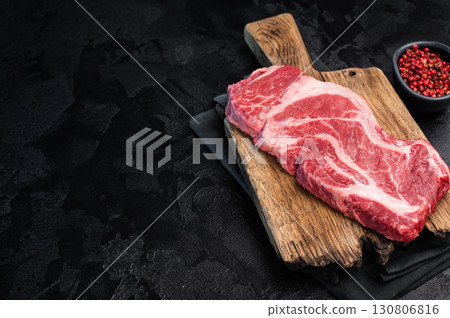 Uncooked Raw Chuck eye roll steak, prime beef meat on wooden board. black background. top view 130806816