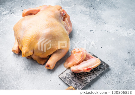 A whole raw chicken and a few chicken pieces lie on a gray countertop 130806838