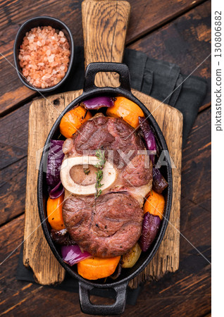 Hearty ossobuco slow cooked to perfection, showcasing succulent osso buco shank meat and aromatic herbs in a comforting stew. wooden background. top view 130806882