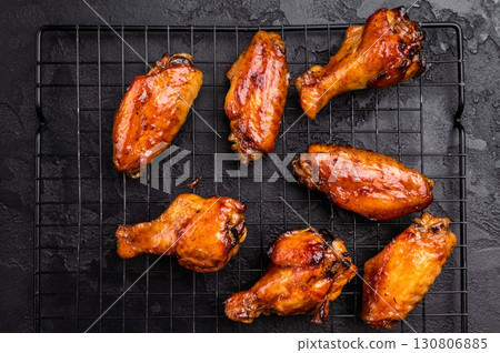Mouthwatering BBQ chicken wings, coated in a rich sauce, perfect for finger-licking appetizers at any gathering. black background. top view Mouthwatering BBQ chicken wings, coated in a rich sauce, perfect for finger-licking appetizers at any gathering. black background. top view 130806885