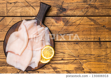 Freshly caught raw squid with glistening skin, perfect for grilling or frying to create mouthwatering dishes. wooden background. top view 130806918