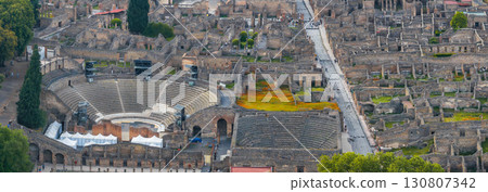 Aerial view of Pompeii ruins in Italy, featuring an amphitheater with semi circular seating, stone buildings, streets, and patches of greenery. Aerial view of Pompeii ruins in Italy, featuring an amphitheater with semi circular seating, stone buildings, streets, and patches of greenery. 130807342