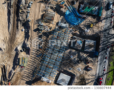 Aerial view of a construction site in Riga, Latvia, featuring a steel framework, workers, machinery, dirt roads, and visible progress on infrastructure. 130807444