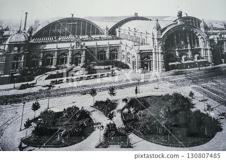 Historic Frankfurt Central Station in Germany features arched windows, intricate facade details, and surrounding pathways with trees in black and white. Historic Frankfurt Central Station in Germany features arched windows, intricate facade details, and surrounding pathways with trees in black and white. 130807485