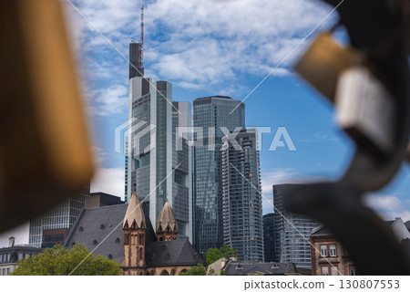 View of Frankfurt, Germany, highlighting a historic building with pointed towers and modern skyscrapers, including the Commerzbank Tower, under a blue sky. 130807553