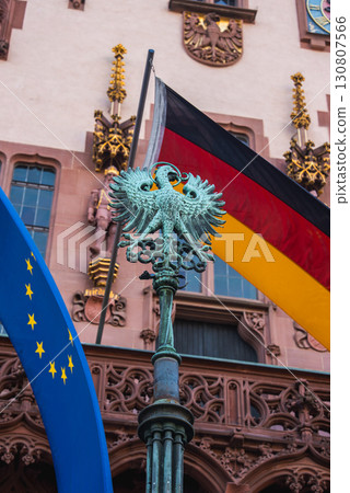 The Romer in Frankfurt, Germany, features ornate architecture, German and EU flags, and a metal sculpture of the German eagle in the foreground. 130807566