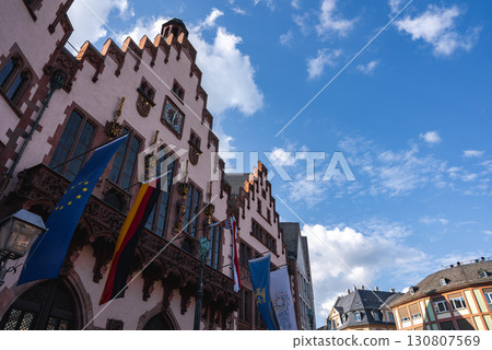 The Romer in Frankfurt, Germany, features stepped gables, a pinkish facade, and a clock. Flags and nearby traditional buildings complete the scene. The Romer in Frankfurt, Germany, features stepped gables, a pinkish facade, and a clock. Flags and nearby traditional buildings complete the scene. 130807569