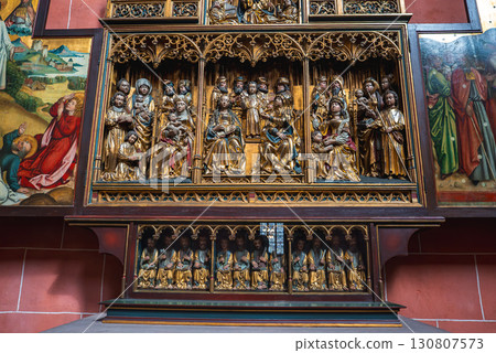 Intricately carved altarpiece in a Frankfurt church, featuring saints, angels, Gothic arches, and painted biblical panels against a red brick wall. 130807573
