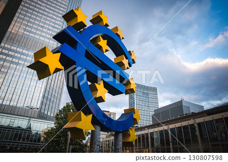 The Euro sculpture in Frankfurt, Germany, surrounded by yellow stars, with modern skyscrapers and the European Central Bank's former headquarters in view. The Euro sculpture in Frankfurt, Germany, surrounded by yellow stars, with modern skyscrapers and the European Central Bank's former headquarters in view. 130807598