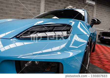 A bright blue Porsche Macan with sleek headlights and glossy finish parked indoors on a red and black checkered floor with a concrete wall and windows. 130807683