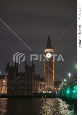 Big Ben clock tower and Westminster Bridge glow against a dark night sky. The River Thames reflects the lights of London's historic architecture. Big Ben clock tower and Westminster Bridge glow against a dark night sky. The River Thames reflects the lights of London's historic architecture. 130807788