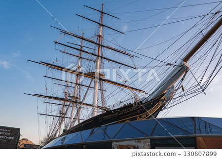 The Cutty Sark, a 19th century clipper ship in Greenwich, London, displays tall masts and rigging above a modern glass structure under a clear blue sky. The Cutty Sark, a 19th century clipper ship in Greenwich, London, displays tall masts and rigging above a modern glass structure under a clear blue sky. 130807899