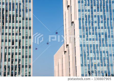 Two glass facade high rise buildings in London with cable cars from the Emirates Air Line system suspended between them under a clear blue sky. 130807905