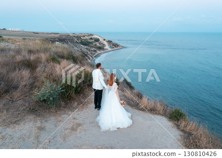 Bride and groom standing on cliff overlooking the sea 130810426