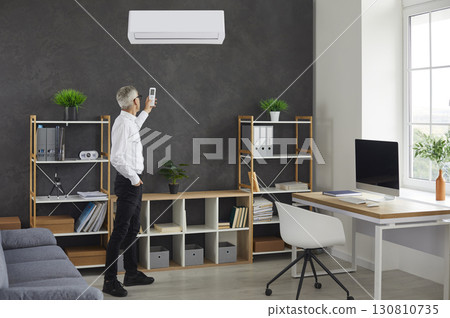 Businessman switching a modern wall mounted air conditioner in his office at work Businessman switching a modern wall mounted air conditioner in his office at work 130810735