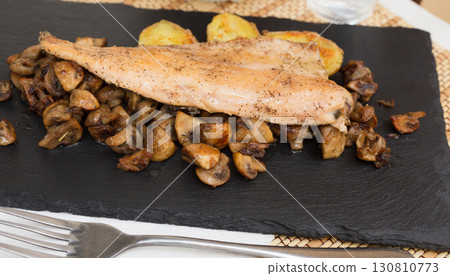fried trout fillet on pillow of fried champignon mushrooms on dark warm stone plate 130810773