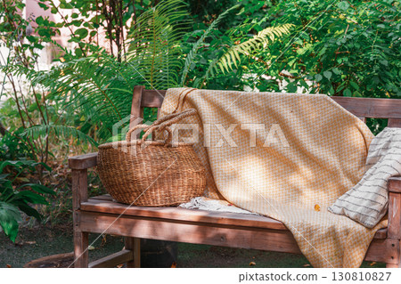 Wooden garden bench with yellow blanket and straw basket, place fo relax in cozy summer backyard Wooden garden bench with yellow blanket and straw basket, place fo relax in cozy summer backyard 130810827