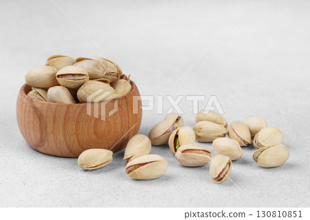 Little wooden bowl with salted pistachio nuts and scattered seeds on gray background close up Little wooden bowl with salted pistachio nuts and scattered seeds on gray background close up 130810851