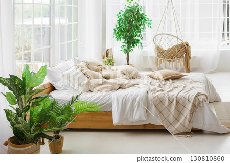 Comfortable bed with lots of soft decorative beige pillows in light sunny bedroom with large window Comfortable bed with lots of soft decorative beige pillows in light sunny bedroom with large window 130810860