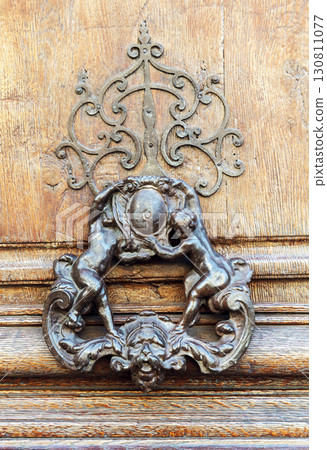 Door knocker featuring intricate design with lion and circular emblem mounted on wooden surface 130811077