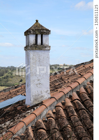 Chimney on a rustic house roof with clay tiles in a rural landscape under blue sky Chimney on a rustic house roof with clay tiles in a rural landscape under blue sky 130811125
