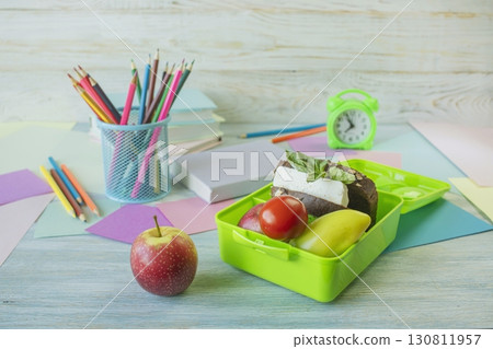 Back to school concept, school food. Lunch box with healthy sandwich, alarm clock, stack of books and  apple on wooden background. 130811957