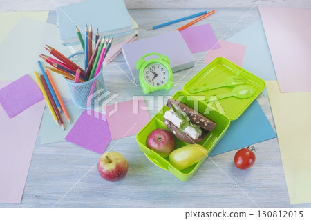 Back to school concept, school food. Lunch box with healthy sandwich, alarm clock, stack of books and apple on white wooden background. Back to school concept, school food. Lunch box with healthy sandwich, alarm clock, stack of books and apple on white wooden background. 130812015
