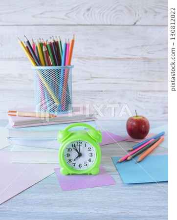 Back to school concept. Alarm clock, stack of books, apple, colored pencils and pastel colored paper on white wooden background. Back to school concept. Alarm clock, stack of books, apple, colored pencils and pastel colored paper on white wooden background. 130812022