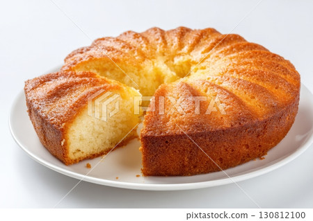 Bundt cake with a crimped top and a glossy sheen on a white plate on a white background. One piece is cut out with soft smooth texture inside. Golden-brown round classic cake and one slice cut out 130812100