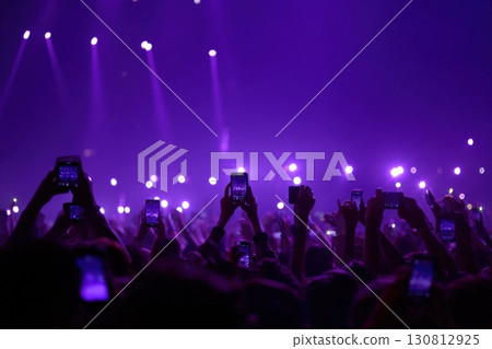 A crowded concert hall with scene stage lights in blue tones, rock show performance, with people silhouette, on dance floor air during a concert festival. Fans with raised arms at music rave party A crowded concert hall with scene stage lights in blue tones, rock show performance, with people silhouette, on dance floor air during a concert festival. Fans with raised arms at music rave party 130812925