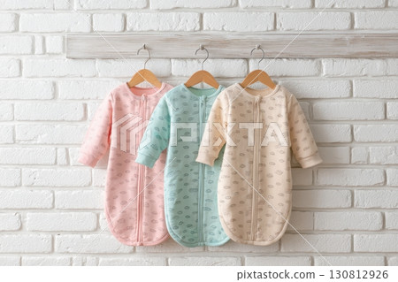 Baby onesie set hanging on a white bricks wall. Fashion newborn clothes. Flat lay, top view. Baby kids soft clothing made from cotton. Infant trendy bodysuit pastel colors, earth tones. Gender neutral 130812926