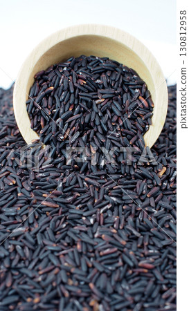Closeup of raw riceberry rice grains in a wooden bowl spilling onto a pile of rice. Perfect for illustrating Thai rice, healthy organic food Closeup of raw riceberry rice grains in a wooden bowl spilling onto a pile of rice. Perfect for illustrating Thai rice, healthy organic food 130812958