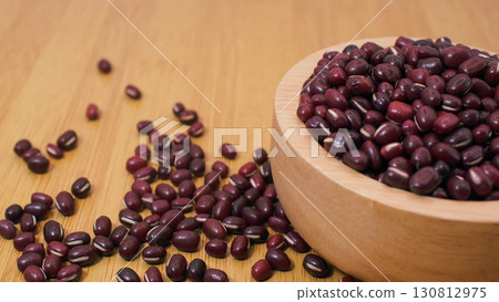 Close-up of red adzuki beans in a wooden bowl with scattered beans on wooden background, symbolizing healthy eating, plant protein, and Asian cuisine ingredients. 130812975
